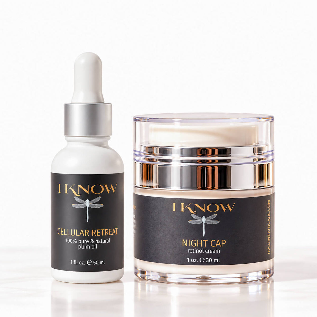 A skincare set from IKnow Cosmetics featuring a white dropper bottle of Cellular Retreat plum oil and a clear jar of Night Cap retinol cream, both with black labels and gold lettering, set against a clean white background.