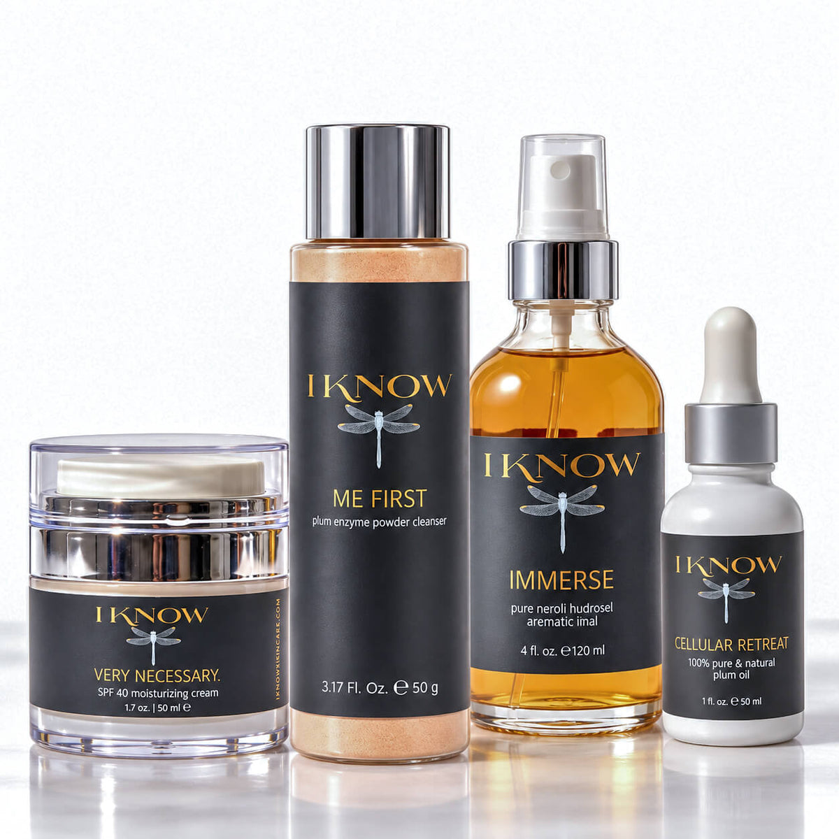 Four skincare products from IKnow Cosmetics arranged on a reflective white surface against a white background: a jar of Very Necessary SPF 40 moisturizing cream, a bottle of Me First exfoliating powder cleanser, a bottle of Immerse pure neroli budget aromatic inhaler, and a dropper bottle of Cellular Retain 100% pure & natural plant serum.
