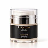 A jar of IKnow Night Cap Retinol Cream on a white background. The product is in a clear glass jar with a silver metallic collar and a black label featuring gold lettering and a dragonfly graphic.